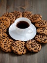 A stack of chocolate chip cookies around coffee cup on a wooden table