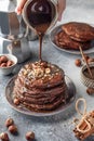 Stack of chocolate pancakes with nuts and chocolate syrup on a ceramic plate, process of pouring syrup on top. Cozy breakfast and Royalty Free Stock Photo