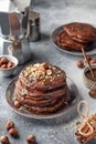 Stack of chocolate pancakes topped with nuts and drizzled with chocolate syrup served on a plate for breakfast, gray background Royalty Free Stock Photo