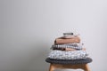 Stack of clean bed linen and pillow on stool near light grey wall. Space for text Royalty Free Stock Photo