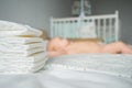Stack of clean diapers on foreground selective focus and baby girl lying on bed white sheets at home on blurred Royalty Free Stock Photo