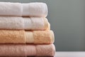 Stack of clean folded white beige terry towels on gray wall background. Laundry spa wellness cleanliness concept