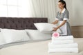 Stack of clean towels with flower on bed and chambermaid in hotel room, closeup. Space for text