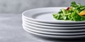 Stack of clean white ceramic plates with fresh green salad leaves and cherry tomatoes on top, placed on a gray textured surface Royalty Free Stock Photo