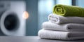 Stack of clean white and green towels folded neatly on a surface with a blurred washing machine in the background Royalty Free Stock Photo