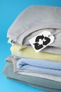 Stack of clothes with recycling label on light blue background, closeup Royalty Free Stock Photo