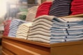 A stack of clothes in the store, pullovers and sweatshirts nicely and neatly stacked in bundles on the table and red