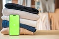 Stack of clothing prepared for resale with a smartphone displaying green screen for mockup use. Mobile apps simplify Royalty Free Stock Photo