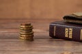 Stack of coin money, holy bible book and old wallet on wooden table, a closeup