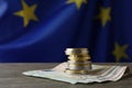 Stack of coins and banknotes on wooden table against European Union flag, space for text Royalty Free Stock Photo