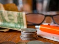 Stack of coins, blurred folded One US dollar banknote, a notepad with a pen and glasses in background and a pile of coins in the Royalty Free Stock Photo