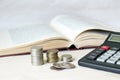 A stack of coins and a calculator in front of an open book. Concept of expensive education and low scholarship