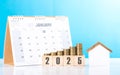 A stack of coins, a house model, and 2025 calendar placed together on a table. Represents the concept of mortgage planning, Royalty Free Stock Photo