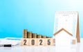 A stack of coins, a house model, and 2025 calendar placed together on a table. Represents the concept of mortgage planning, Royalty Free Stock Photo