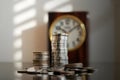 Stack of coins in front of blurred clock symbolizing finance, savings, or time concept Royalty Free Stock Photo