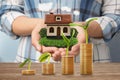 Stack of coins on wooden table and woman holding house model. Real estate investing Royalty Free Stock Photo