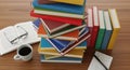Stack of colorful books coffee cup and papers on a wooden table top view ready for reading and learning white background Royalty Free Stock Photo