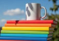 Stack of colorful books with a white mug on top against blue sky Royalty Free Stock Photo