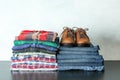 Stack of colorful shirts, jeans and shoes on table against light background