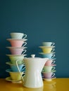 Stack of colorful vintage tea and coffee cups and tea pot on yellow table against petrol background. Vertical. Royalty Free Stock Photo