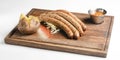 Stack of cooked sausages served on a rustic wooden board with sauce and baked potatoes.