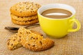 Stack of cookies with sesame and flax seeds, spoon, broken cookie, cup of coffee with milk on mat Royalty Free Stock Photo