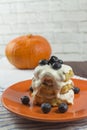 A stack of cottage cheese pancakes with sour cream and blueberries on an orange plate, side view