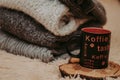 Stack of cozy knitted clothes on a soft carpet. Mug on a wooden stand