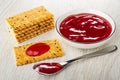 Stack of crackers with flax seeds, bowl with cherry jam, cookie poured jam, spoon with jam on wooden table Royalty Free Stock Photo