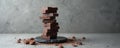 Stack of dark chocolate pieces balanced on slate plate. Cocoa powder sprinkles around broken chunks on concrete surface. Studio Royalty Free Stock Photo