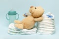 Stack of diapers with cute teddy bear,toy pacifier bottle lying on table. set for infant newborn boy girl for baby shower present Royalty Free Stock Photo