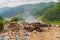 Stack of different types of large garbage dump, plastic bags, and trash burning near paddy rice terraces, agricultural fields of