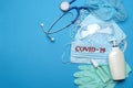 Stack of Disposable blue medical face masks with COVID-19 sign, rubber latex gloves, goggles, stethoscope and alcohol