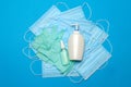 Stack of Disposable blue medical face masks, rubber latex gloves and alcohol hand sanitizer antiseptic on blue