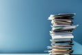 Stack of documents leaning unevenly on desk with blue wall background and light reflecting off surface creating shadows and Royalty Free Stock Photo