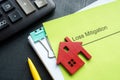 A stack of documents about loss mitigation with a figurine of a house.