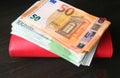 Stack of Euro banknotes on red wallet isolated on black wooden background Royalty Free Stock Photo