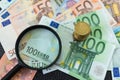 Stack of Euro coins on pile of banknotes with magnifying glass a