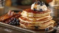 A stack of fluffy pancakes topped with maple syrup whipped cream and fresh blueberries served alongside a tray of bacon Royalty Free Stock Photo