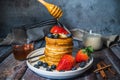 A stack of fluffy soft pancakes with pouring maple syrup from stick, fresh blueberry, strawberry and a glass of milk on wooden Royalty Free Stock Photo