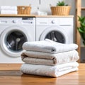 Stack of fluffy white and beige towels on a wooden table with two washing machines in the background Royalty Free Stock Photo