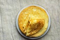 Stack of folded delicious freshly baked crepes with appetizing golden crust on white plate on linen table cloth. Cozy atmosphere