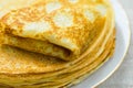 Stack of folded delicious freshly baked crepes with appetizing golden crust on white plate on linen table cloth by window