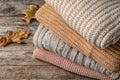 Stack of folded knitted sweaters and autumn leaves