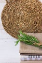 Stack of folded linen towels wicker rattan coaster on white wood background, twig of rosemary, kitchen interior