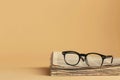 A stack of folded newspapers with black eyeglasses resting on top. The background is a plain beige color. Generative AI Royalty Free Stock Photo