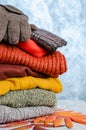 Stack of folded warm knitted women`s sweaters, scarf, gloves in warm colors and bright autumn leaves. Copy space Royalty Free Stock Photo