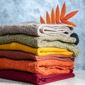 Stack of folded warm knitted women`s sweaters in warm colors and bright autumn leaves on gray background. Copy space Royalty Free Stock Photo