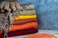 Stack of folded knitted women`s sweaters in warm colors, scarf, gloves and autumn leaves on gray background. Copy space Royalty Free Stock Photo