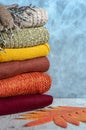 Stack of folded knitted women`s sweaters in warm colors, scarf, gloves and autumn leaves on gray background. Copy space Royalty Free Stock Photo